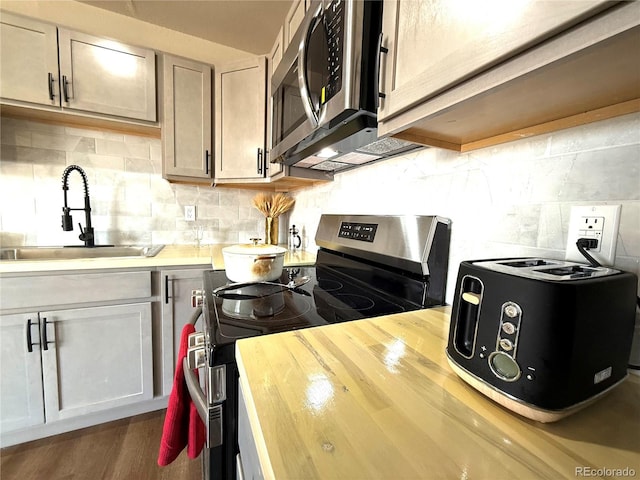 kitchen with backsplash, appliances with stainless steel finishes, wood finished floors, a sink, and wood counters