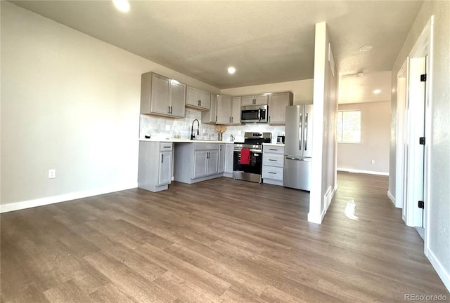 kitchen with wood finished floors, a sink, baseboards, light countertops, and stainless steel appliances