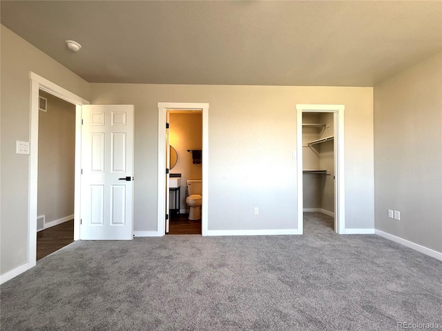 unfurnished bedroom with dark colored carpet, baseboards, a walk in closet, and visible vents