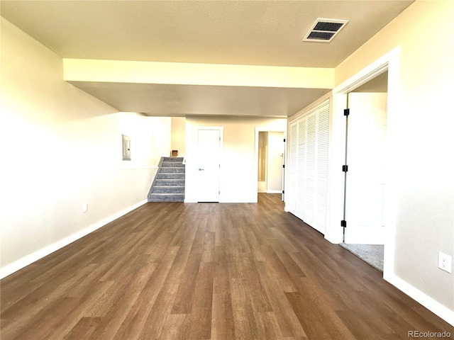 empty room featuring dark wood-style flooring, baseboards, visible vents, and electric panel