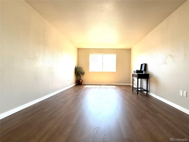 unfurnished living room featuring baseboards, a textured wall, and dark wood-type flooring