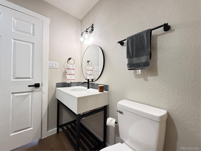 half bathroom featuring vanity, a textured wall, toilet, and wood finished floors