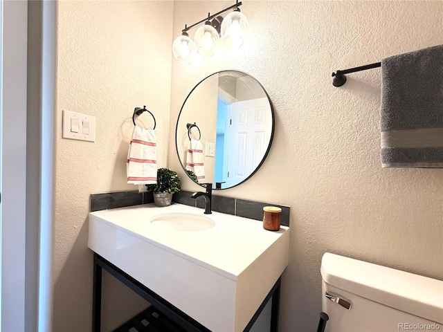 half bath featuring vanity, a textured wall, and toilet