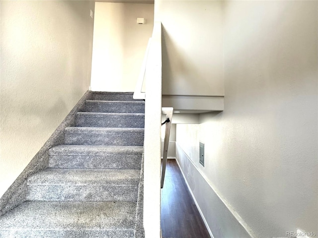 stairway featuring baseboards, a textured wall, and wood finished floors
