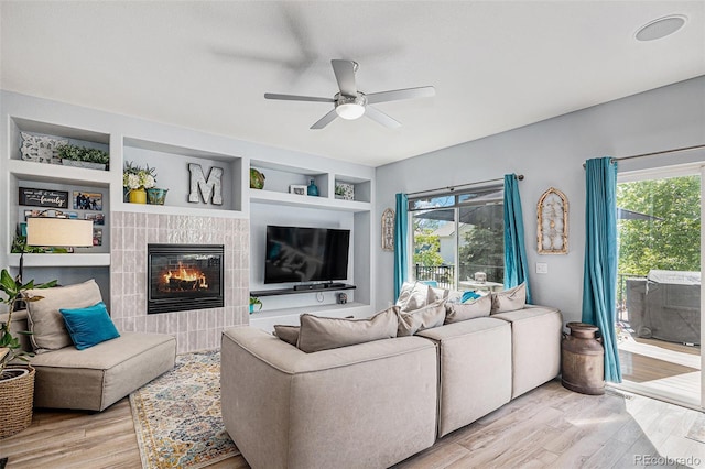 6039 S Ukraine Cir, Aurora, CO 80015 - living area featuring a ceiling fan, light wood-style flooring, a tiled fireplace, and healthy amount of natural light