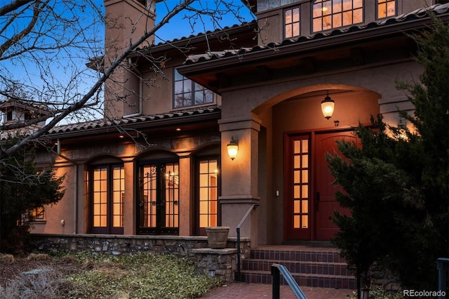 view of exterior entry featuring stucco siding, a chimney, and french doors