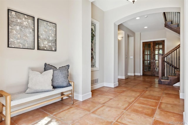 foyer featuring baseboards, stairs, visible vents, and arched walkways