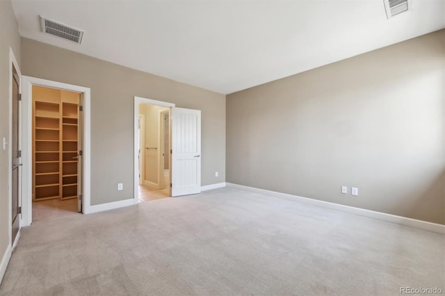 unfurnished bedroom with carpet floors, a walk in closet, visible vents, and baseboards