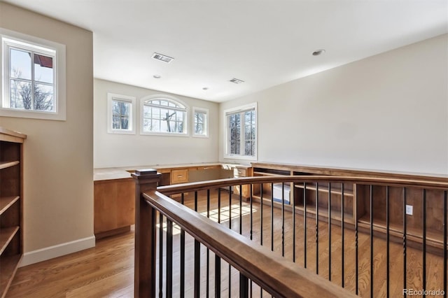 corridor with light wood finished floors, baseboards, visible vents, and an upstairs landing