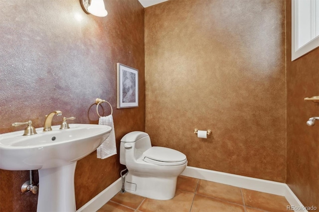 half bath with toilet, baseboards, a sink, and tile patterned floors