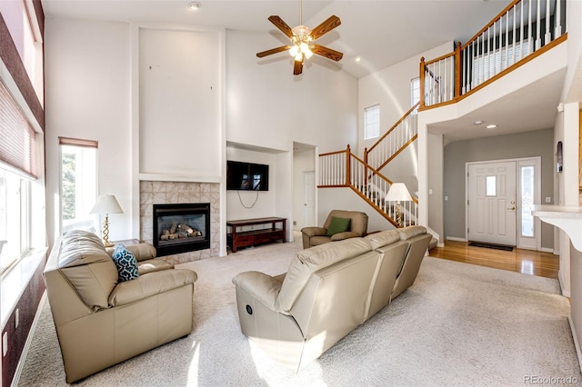 living room featuring a towering ceiling, plenty of natural light, a tiled fireplace, and light hardwood / wood-style floors