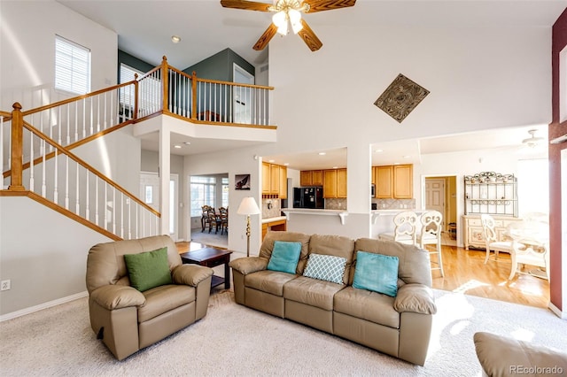 living room with a towering ceiling, ceiling fan, and light wood-type flooring