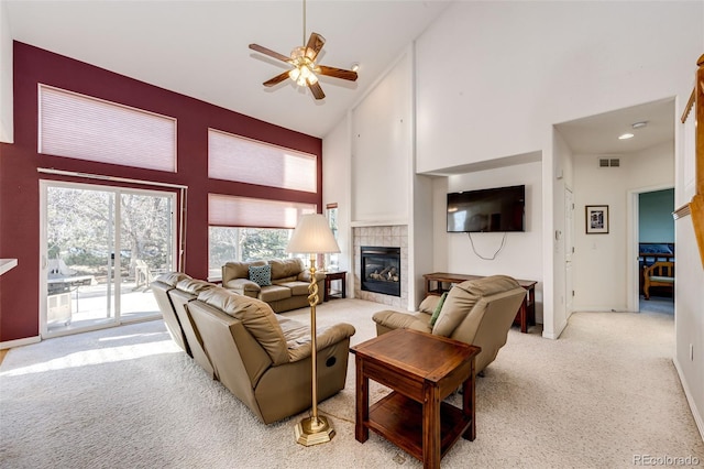 living room with ceiling fan, light colored carpet, a tiled fireplace, and high vaulted ceiling