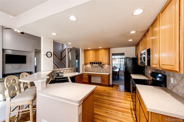 kitchen featuring sink, light hardwood / wood-style flooring, black range with electric stovetop, a kitchen breakfast bar, and kitchen peninsula