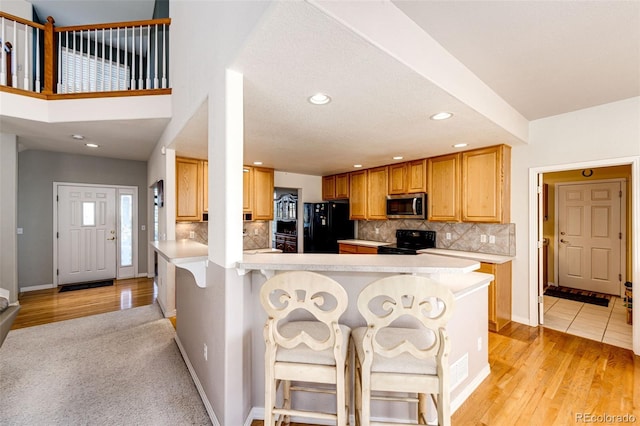 kitchen with light hardwood / wood-style flooring, a breakfast bar area, kitchen peninsula, and black appliances