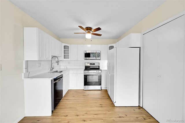 kitchen with tasteful backsplash, glass insert cabinets, stainless steel appliances, a ceiling fan, and a sink