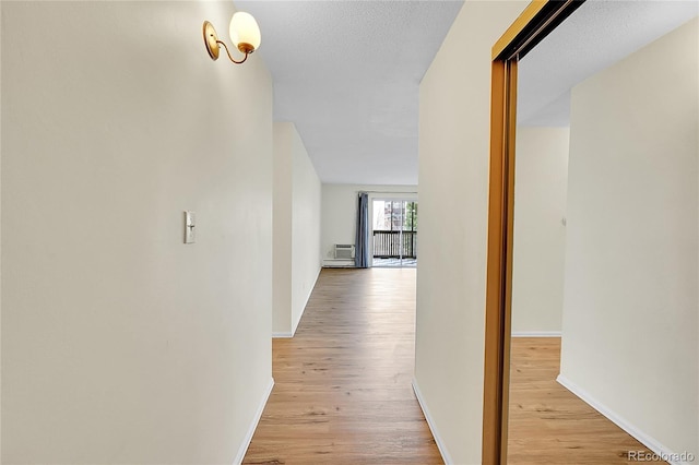 hall with light wood-style flooring, baseboards, and a textured ceiling