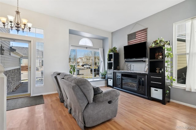 living area with light wood finished floors, a glass covered fireplace, baseboards, and an inviting chandelier