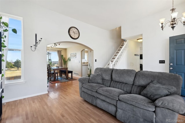 living area with visible vents, arched walkways, light wood finished floors, a chandelier, and stairs