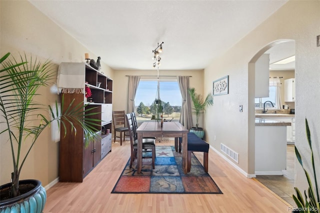 dining room with arched walkways, visible vents, light wood finished floors, and baseboards