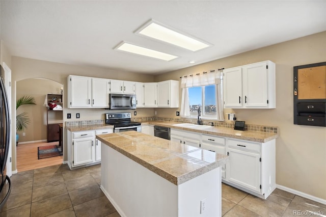 kitchen featuring tile patterned floors, a sink, a center island, appliances with stainless steel finishes, and white cabinets