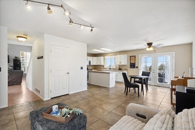 tiled living room featuring visible vents, baseboards, ceiling fan, french doors, and a sink