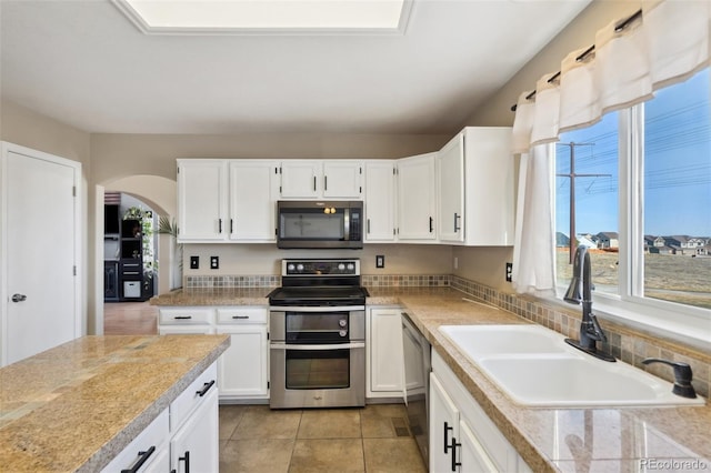 kitchen featuring a sink, stainless steel appliances, arched walkways, and light countertops