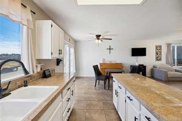 kitchen with a sink, backsplash, white cabinets, light countertops, and light tile patterned floors