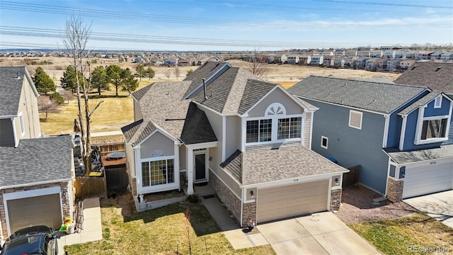 traditional home with a garage, stone siding, roof with shingles, and concrete driveway