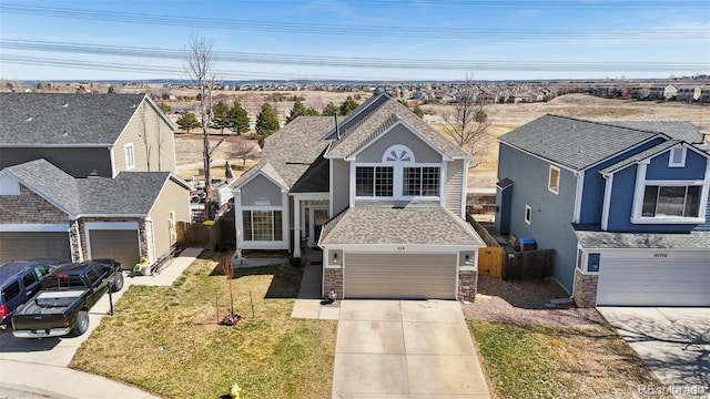 traditional-style home with fence, a shingled roof, concrete driveway, a front lawn, and stone siding