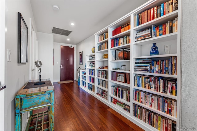 living area featuring wood finished floors, wall of books, and visible vents