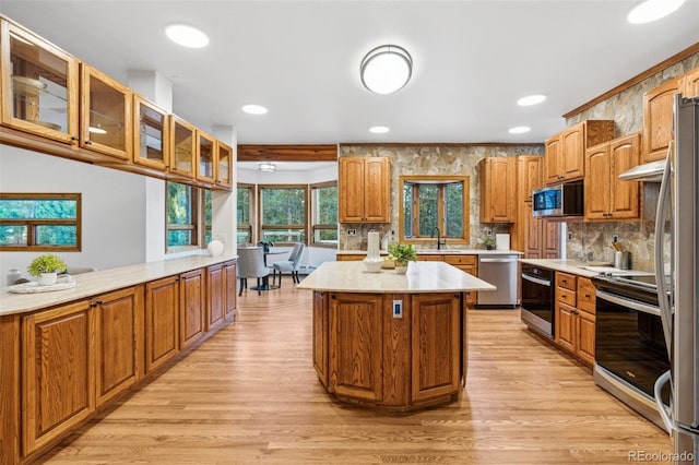 kitchen with sink, tasteful backsplash, a kitchen island, stainless steel appliances, and light hardwood / wood-style floors