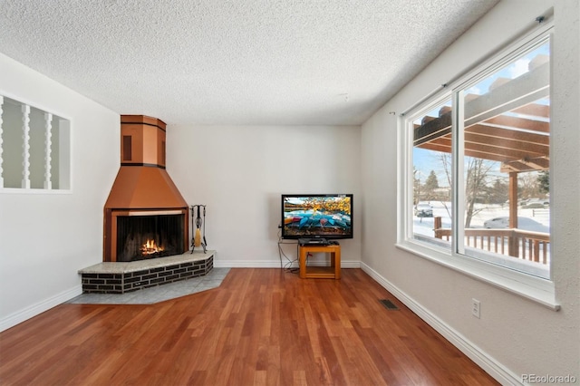 unfurnished living room featuring hardwood / wood-style flooring, a brick fireplace, and a textured ceiling