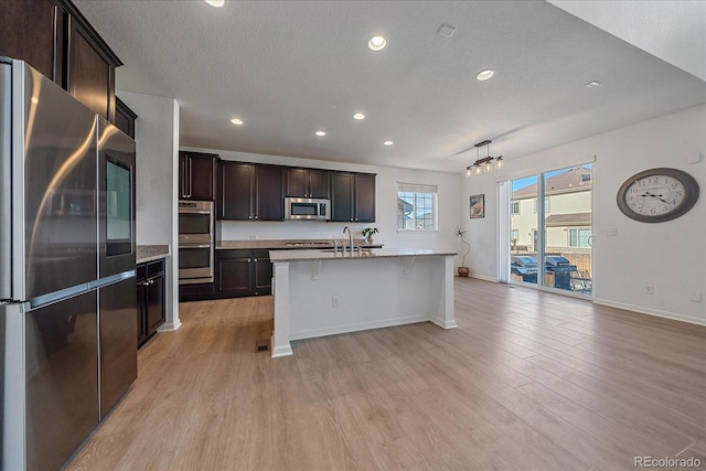 kitchen with light hardwood / wood-style flooring, appliances with stainless steel finishes, sink, a breakfast bar, and a center island with sink