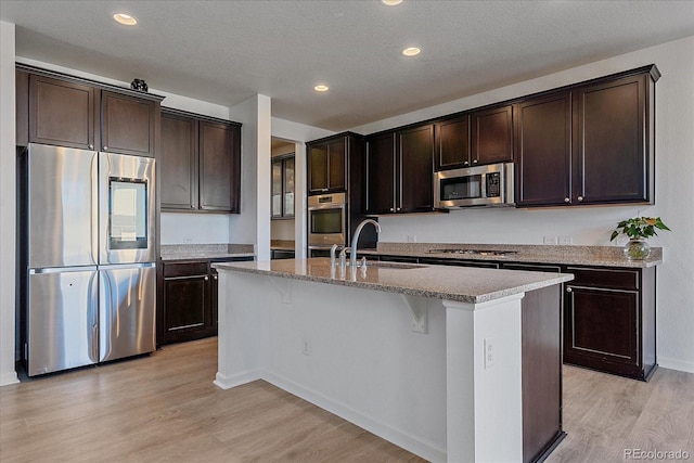 kitchen with light hardwood / wood-style floors, sink, dark brown cabinetry, stainless steel appliances, and a center island with sink