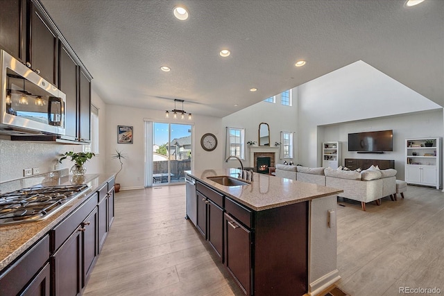 kitchen with stainless steel appliances, light hardwood / wood-style floors, sink, a kitchen island with sink, and a brick fireplace