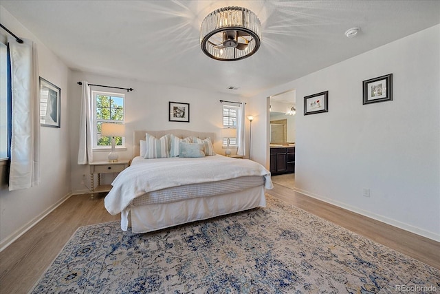 bedroom with light wood-type flooring, connected bathroom, and multiple windows