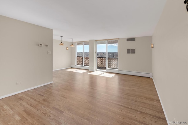 empty room featuring a baseboard heating unit, light hardwood / wood-style flooring, and a wall of windows