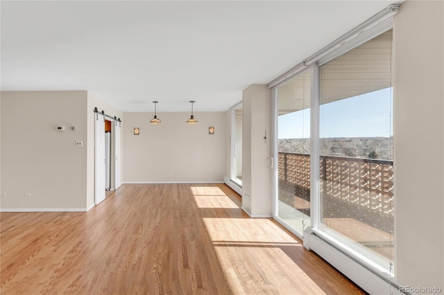 unfurnished room featuring a baseboard heating unit, a barn door, expansive windows, and light wood-type flooring