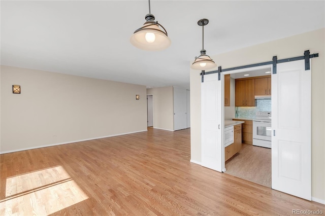 kitchen with backsplash, hanging light fixtures, white appliances, a barn door, and light wood-type flooring