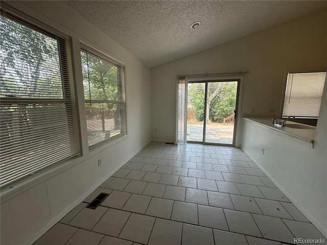 spare room featuring tile patterned flooring, vaulted ceiling, a healthy amount of sunlight, and a textured ceiling