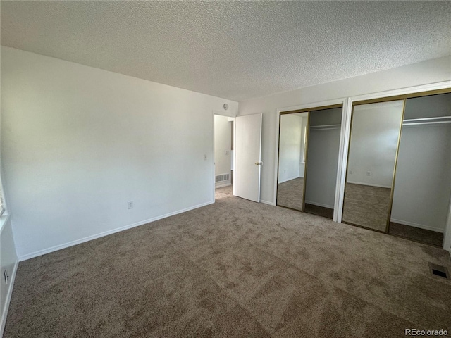 unfurnished bedroom with a textured ceiling, multiple closets, and carpet flooring