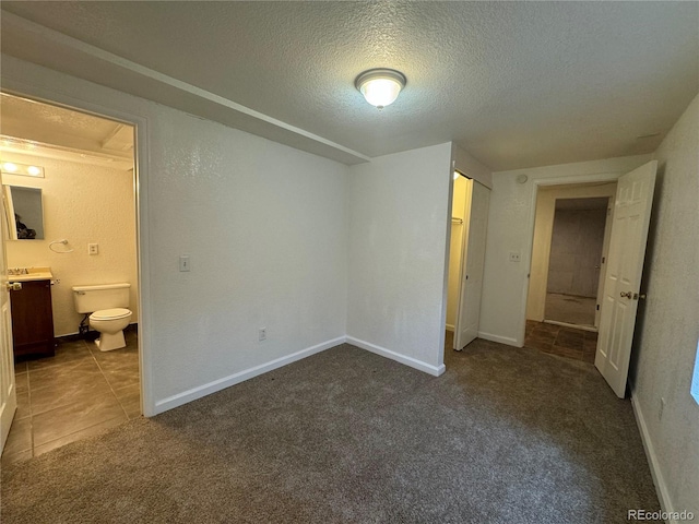 unfurnished bedroom featuring dark colored carpet, connected bathroom, and a textured ceiling