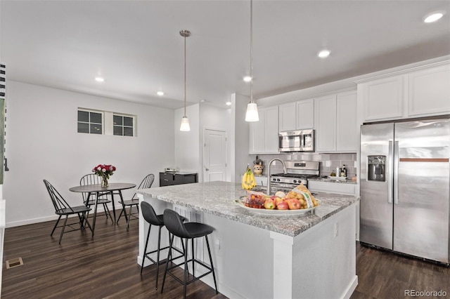 kitchen featuring dark wood-style flooring, light stone counters, visible vents, a kitchen island with sink, and appliances with stainless steel finishes