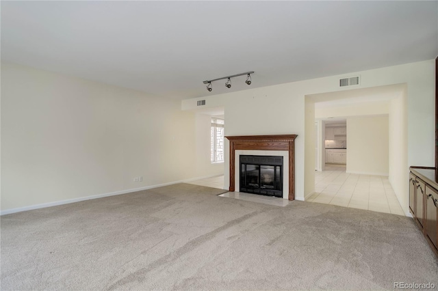 unfurnished living room featuring a fireplace with flush hearth, light colored carpet, visible vents, and rail lighting