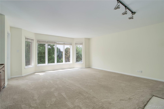 spare room with baseboards, rail lighting, and light colored carpet