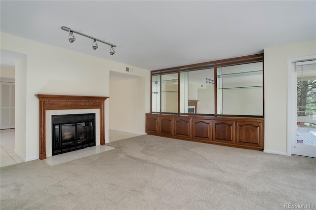 unfurnished living room with a fireplace with flush hearth, rail lighting, light colored carpet, and visible vents