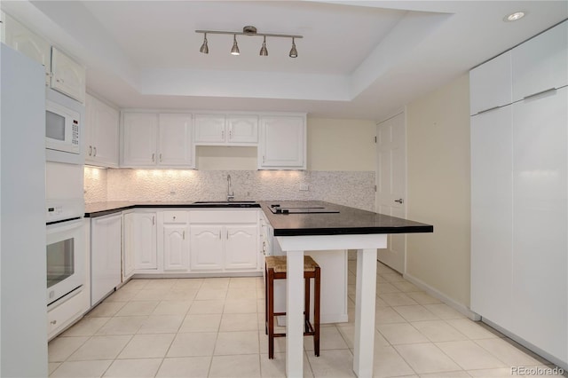 kitchen featuring a raised ceiling, white appliances, backsplash, and a sink