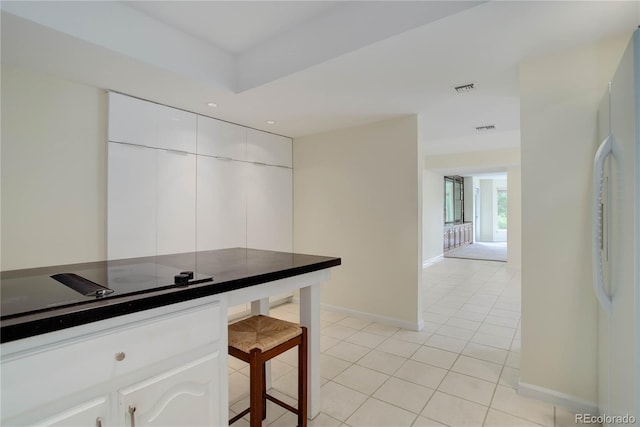 kitchen with light tile patterned floors, visible vents, freestanding refrigerator, white cabinetry, and black electric cooktop