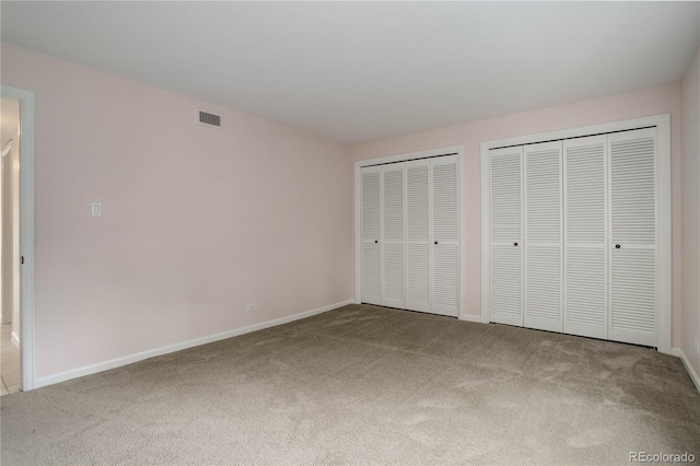 unfurnished bedroom featuring baseboards, visible vents, carpet flooring, and two closets